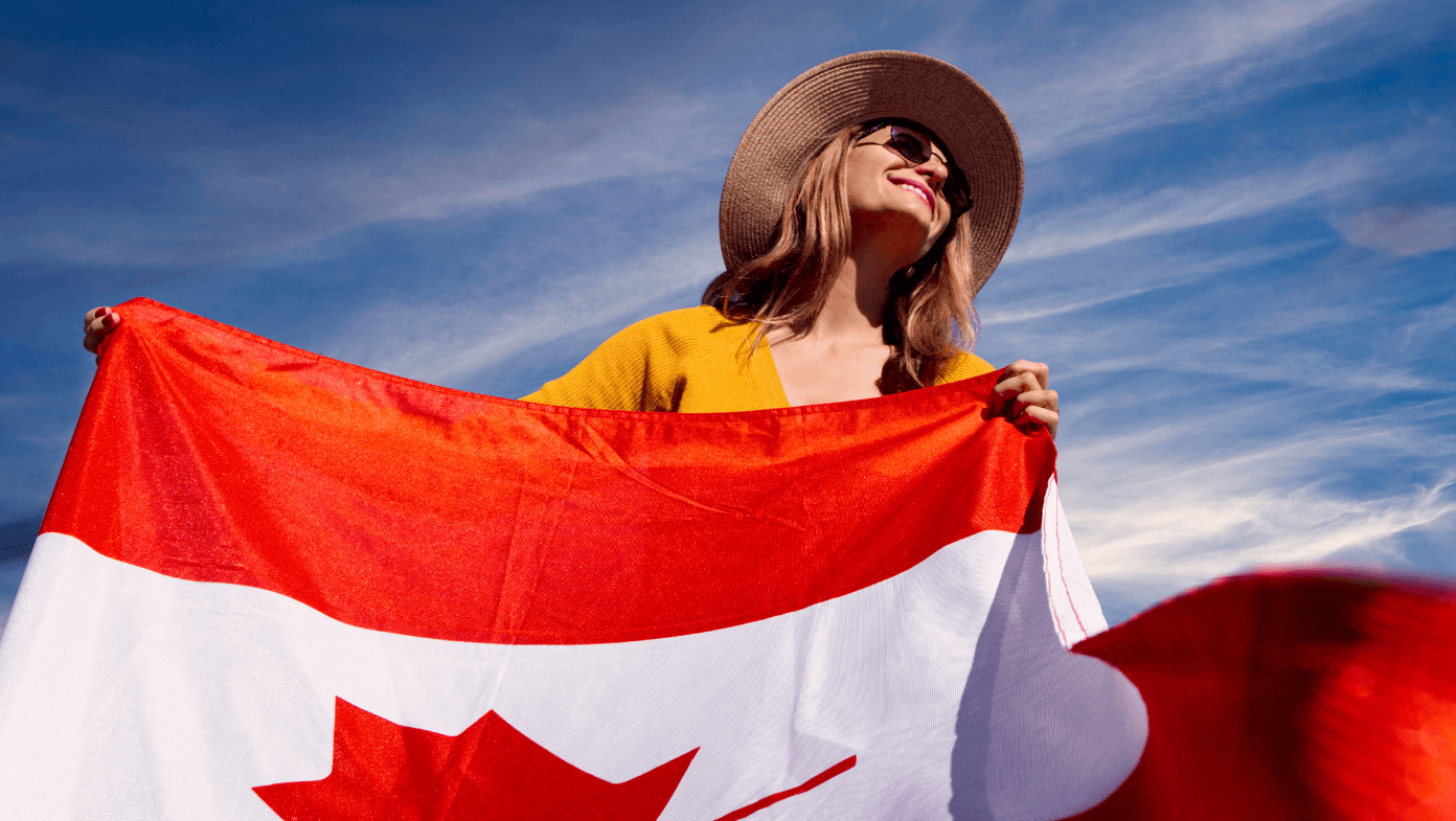 Cheerful woman proudly waving a Canadian flag in front of a vibrant blue sky.