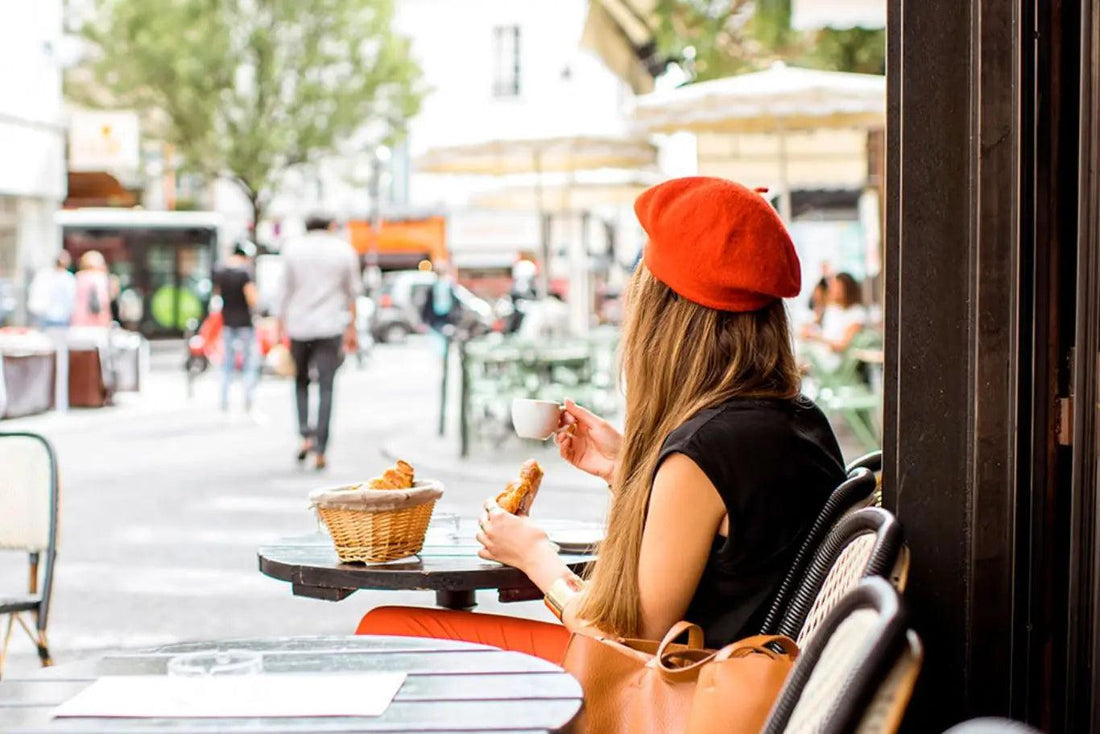 An image of a woman sitting in a coffee shop wearing a red beret, looking relaxed and content. 
