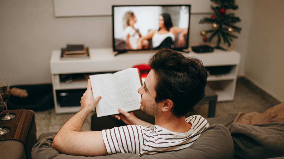 A man reading a book while watching tv