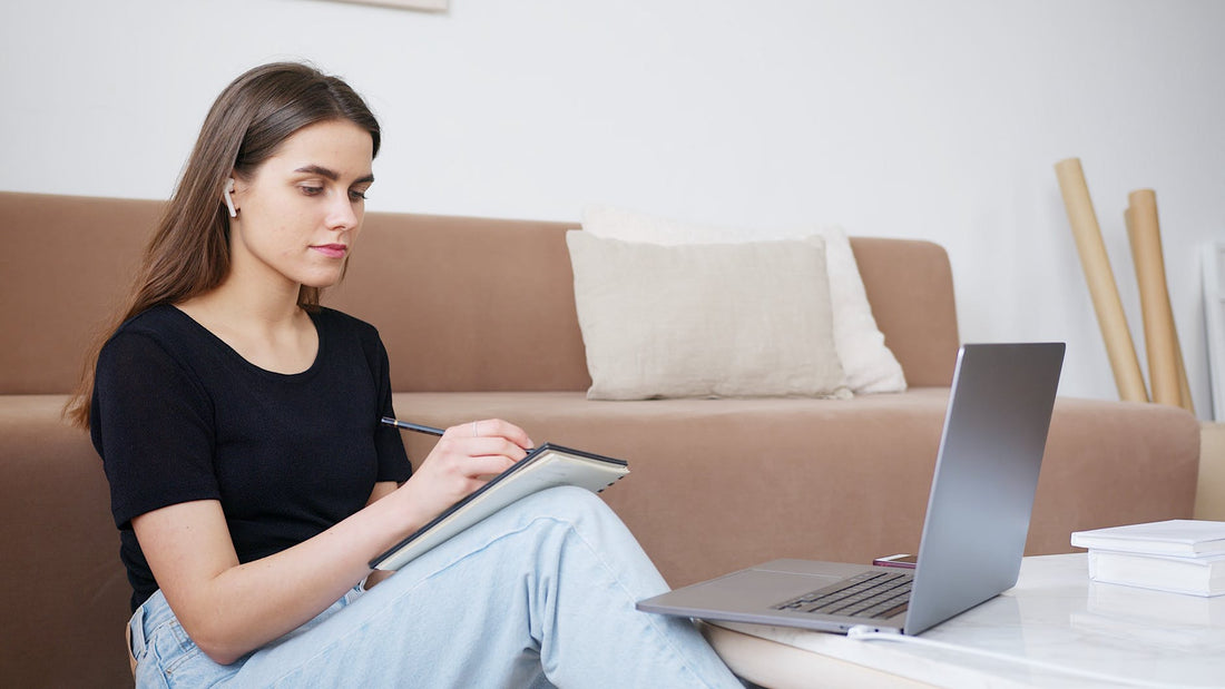 A girl studying with a notebook and laptop, taking notes and focused on her work
