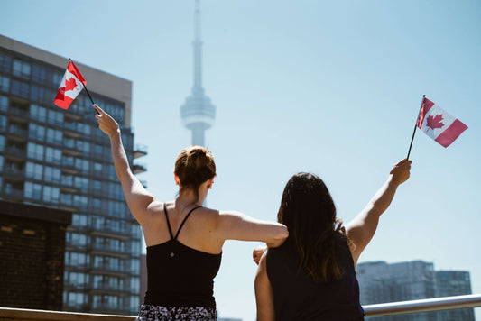 Two women holding a Canadian flag with the CN Tower in the background.