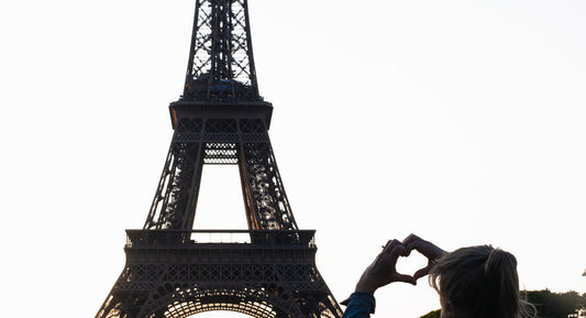 Eiffel Tower in the background with a woman making a heart shape with her hands