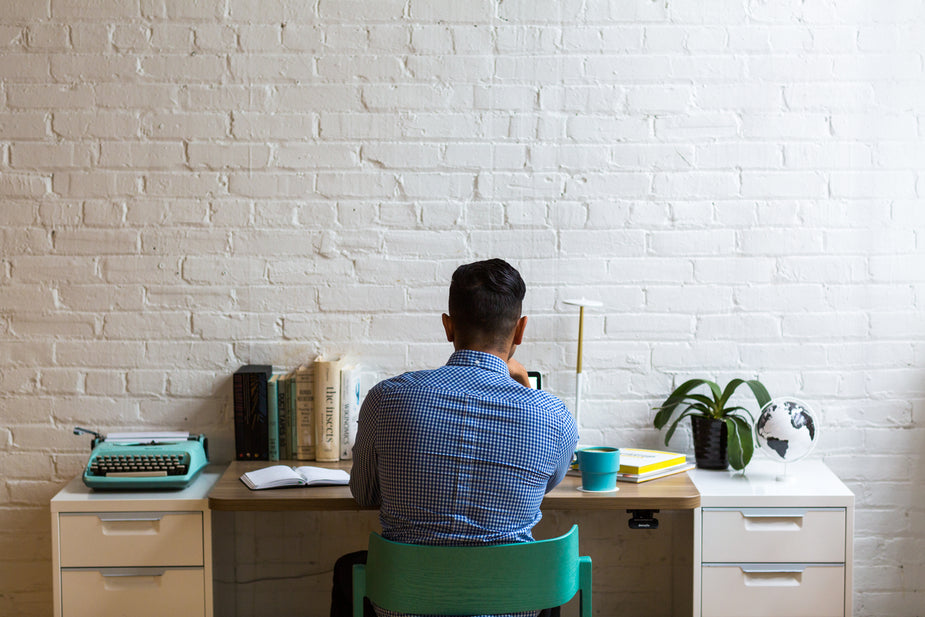 View from behind a man in a blue shirt working at a desk.