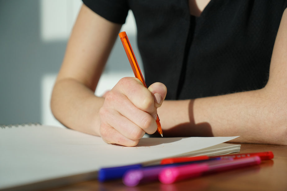 A student writes in a notebook with brightly colored pens.