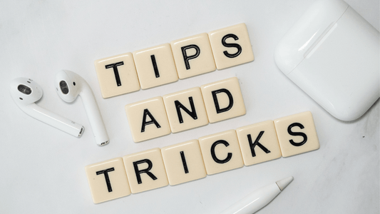 Scrabble tiles spelling Tips and Tricks next to white wireless earbuds on a white surface.