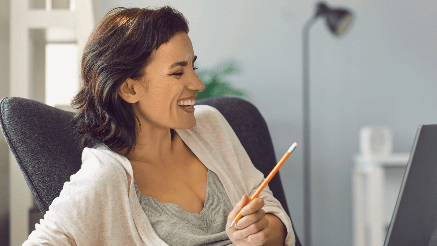 Smiling female student holding a pen, focused on her screen during an online French class.